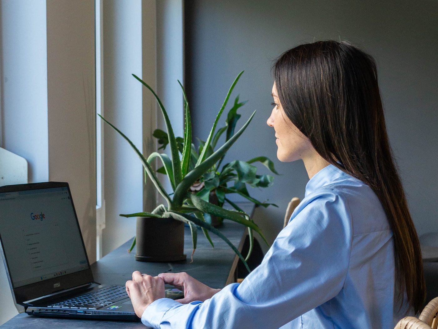 Frau mit langen dunklen Haaren tippt an einem Laptop am Fensterplatz im Womenmatic Space
